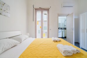 Quarto de hotel com uma cama, um espalha cama amarelo e um conjunto de toalhas.
