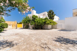 Une cour avec un bâtiment blanc, des arbres et un sol pavé.