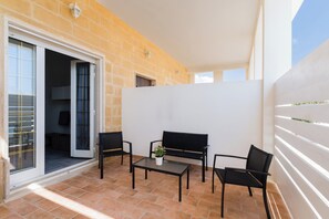 Une terrasse extérieure avec une table et des chaises, un pot de fleurs et une porte-fenêtre coulissante donnant sur un espace intérieur.