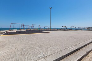 Un parque infantil vacío con columpios y un tobogán, una zona pavimentada y un poste de luz alto.
