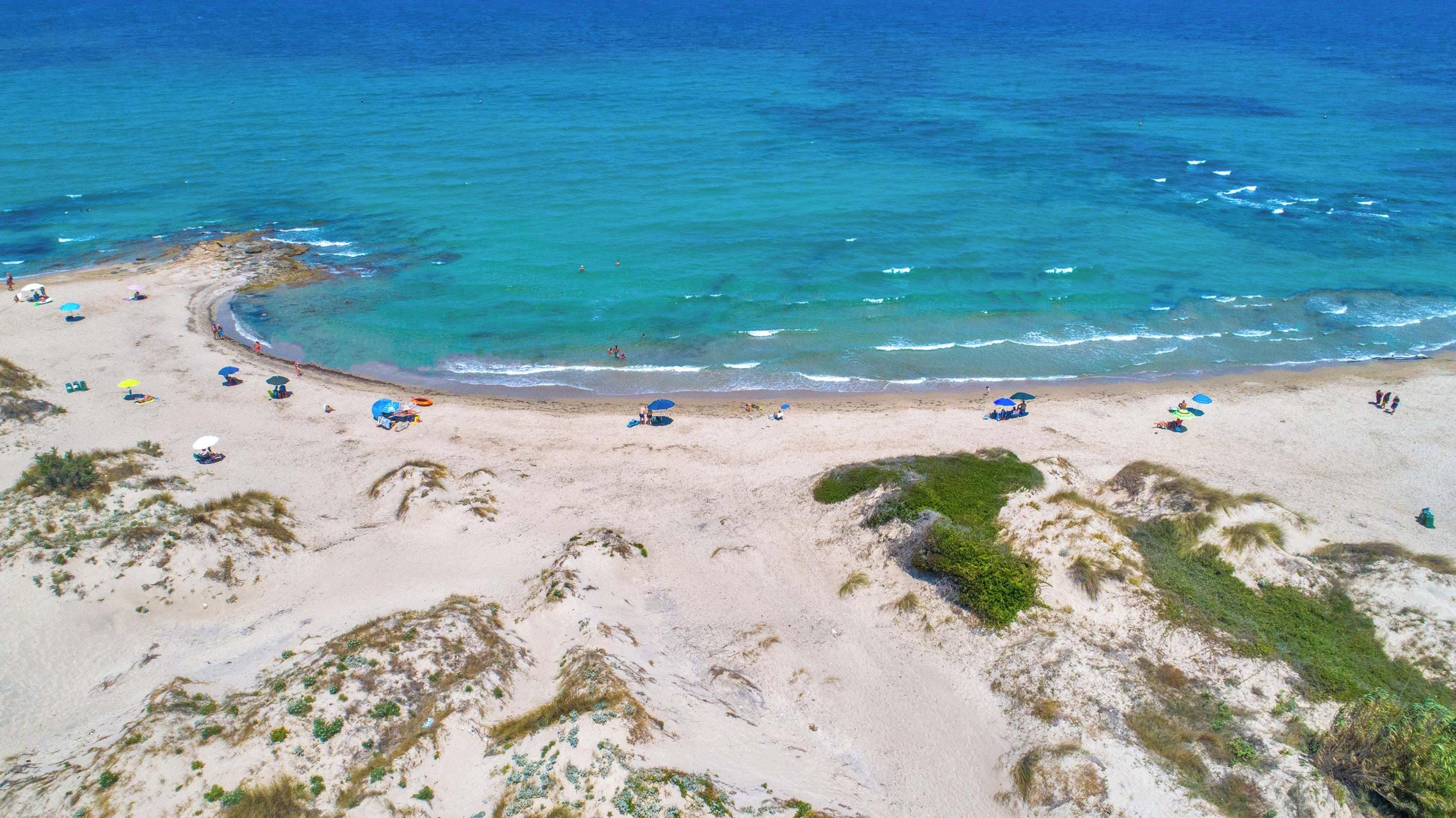 An aerial view of a beach with clear turquoise waters, sandy shores, and scattered umbrellas.