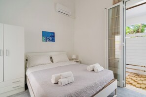 Un dormitorio con cama, armario, un cuadro y vistas a través de un ventanal.