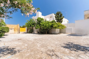 A courtyard with a white building, trees, and a paved ground. - Residence La Baia-Trilo PP Standard by BarbarHouse (Casalabate)