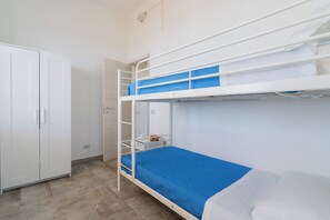 Ein Stockbett mit blauer Matratze, ein weißer Kleiderschrank und ein kleiner Tisch mit Tasse und Schüssel.