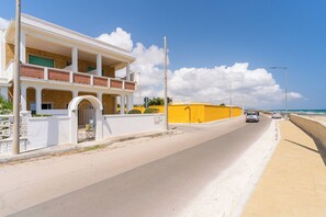 Eine Küstenstraße mit einem zweistöckigen Gebäude, das einen Balkon, eine gelbe Fassade und einen klaren Blick aufs Meer bietet.