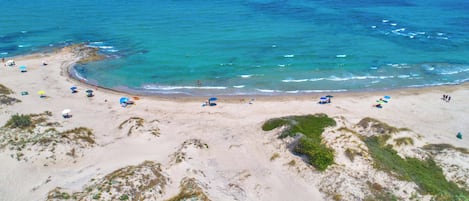 An aerial view of a beach with clear turquoise waters, sandy shores, and scattered umbrellas.