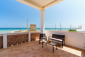 En balkon med et bord og stole, der ud til en strand og et historisk tårn.