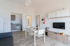 Eine moderne Küche mit Einbauofen und Mikrowelle, ein Essbereich mit Tisch und Stühlen, eine Sitzecke und ein an der Wand befestigter Fernseher.