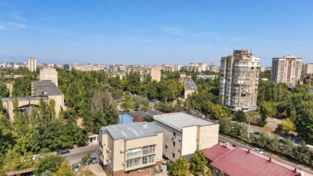Un edificio de gran altura con varios pisos, rodeado de vegetación y otros edificios.
