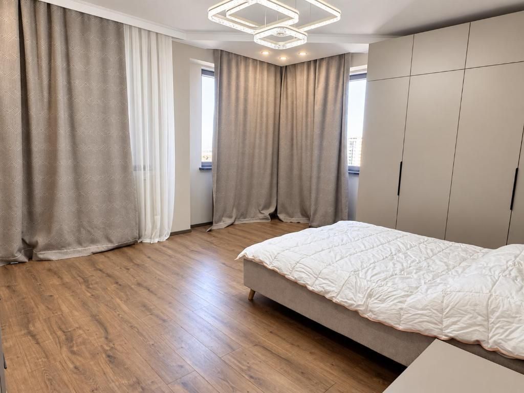 A bedroom with a bed, wooden flooring, curtains, and a wardrobe.
