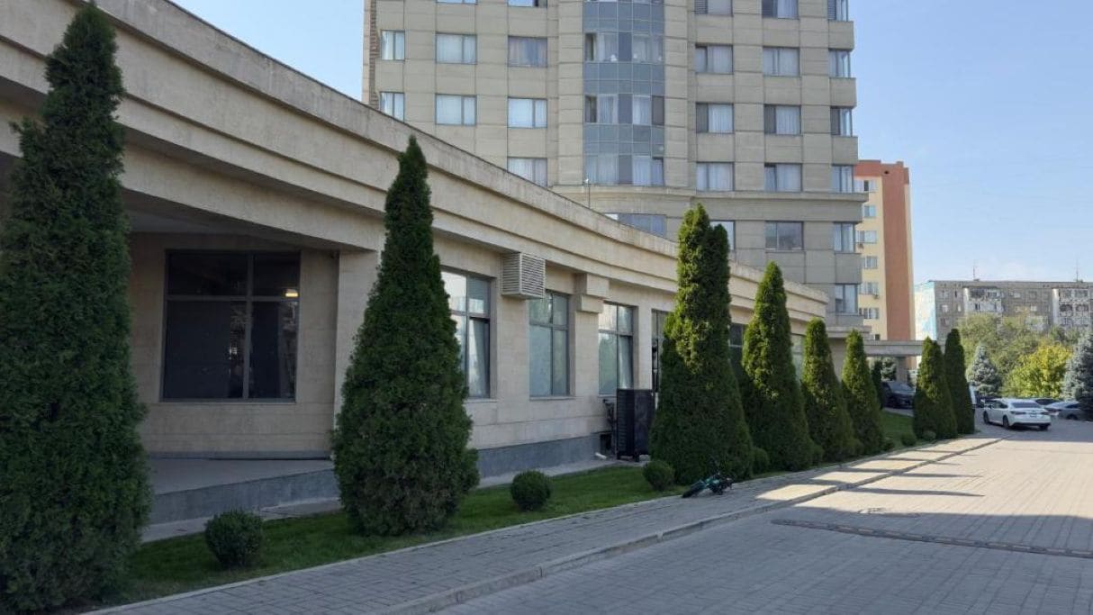 Un edificio moderno con fachada plana, amplias ventanas y un área de entrada pavimentada.