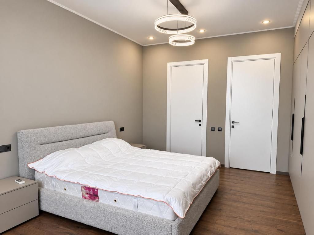 Un dormitorio con cama, dos puertas, una mesita de noche e iluminación moderna.