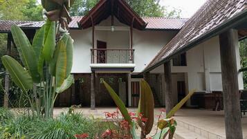 A two-story building with a balcony, surrounded by tropical plants and a tiled roof.