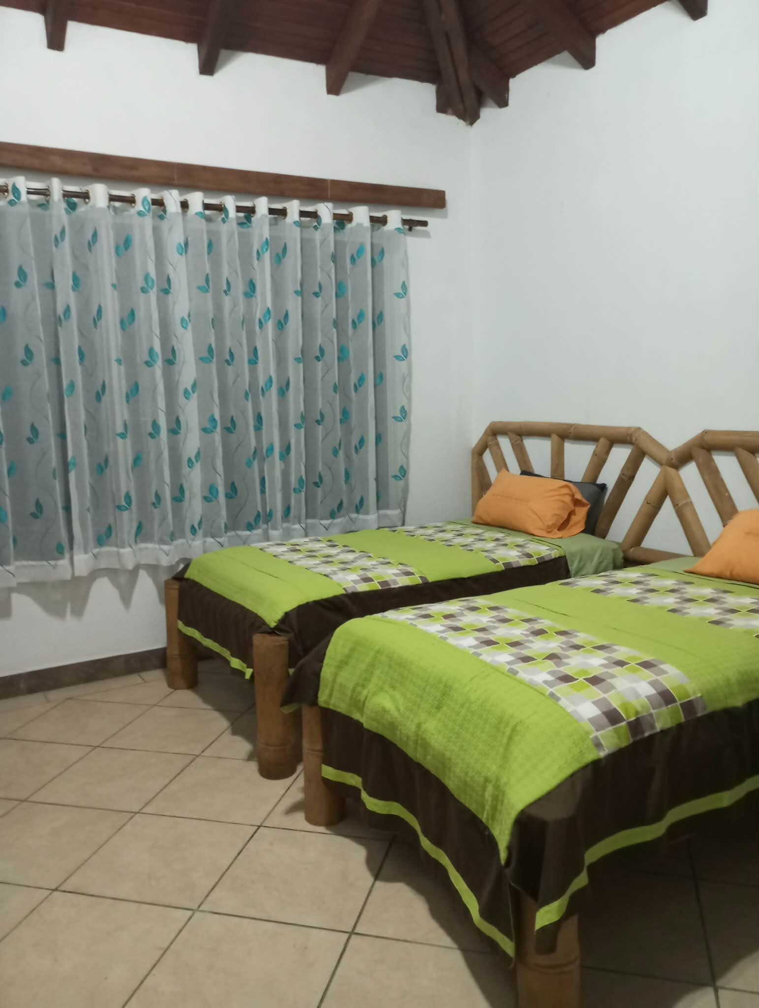 A room with two beds, a window with curtains, and a tiled floor.