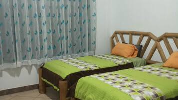 A room with two beds, a window with curtains, and a tiled floor.