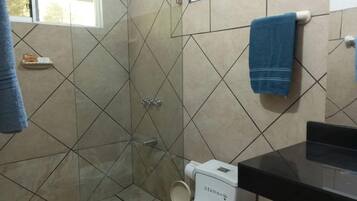 Un baño con cabina de ducha de vidrio, inodoro blanco y lavamanos negro.