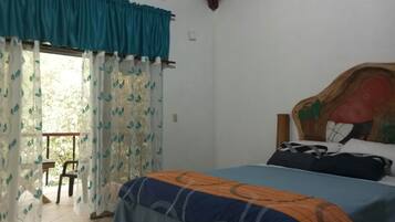 Un dormitorio con cama, una silla, un ventanal con cortinas y techo de madera.