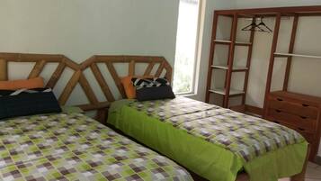 A room with two beds, a wooden wardrobe, and a window.