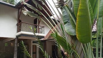 A two-story building with a balcony, surrounded by tropical plants.
