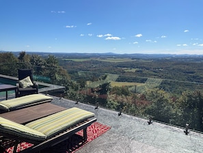A terrace with a view of a valley, a pool, and outdoor seating.