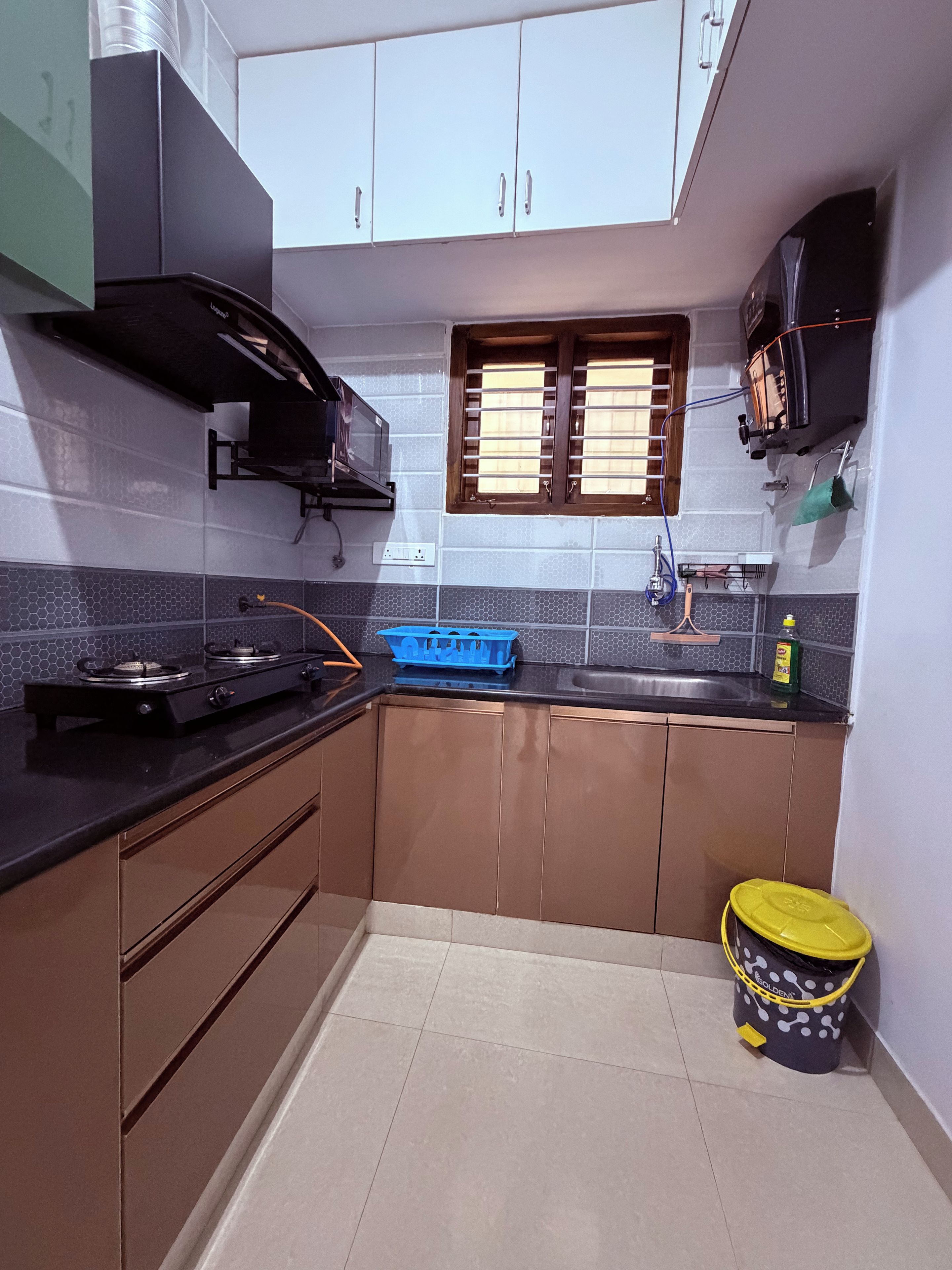 A compact kitchen with a gas stove, a microwave, and a window with blinds.