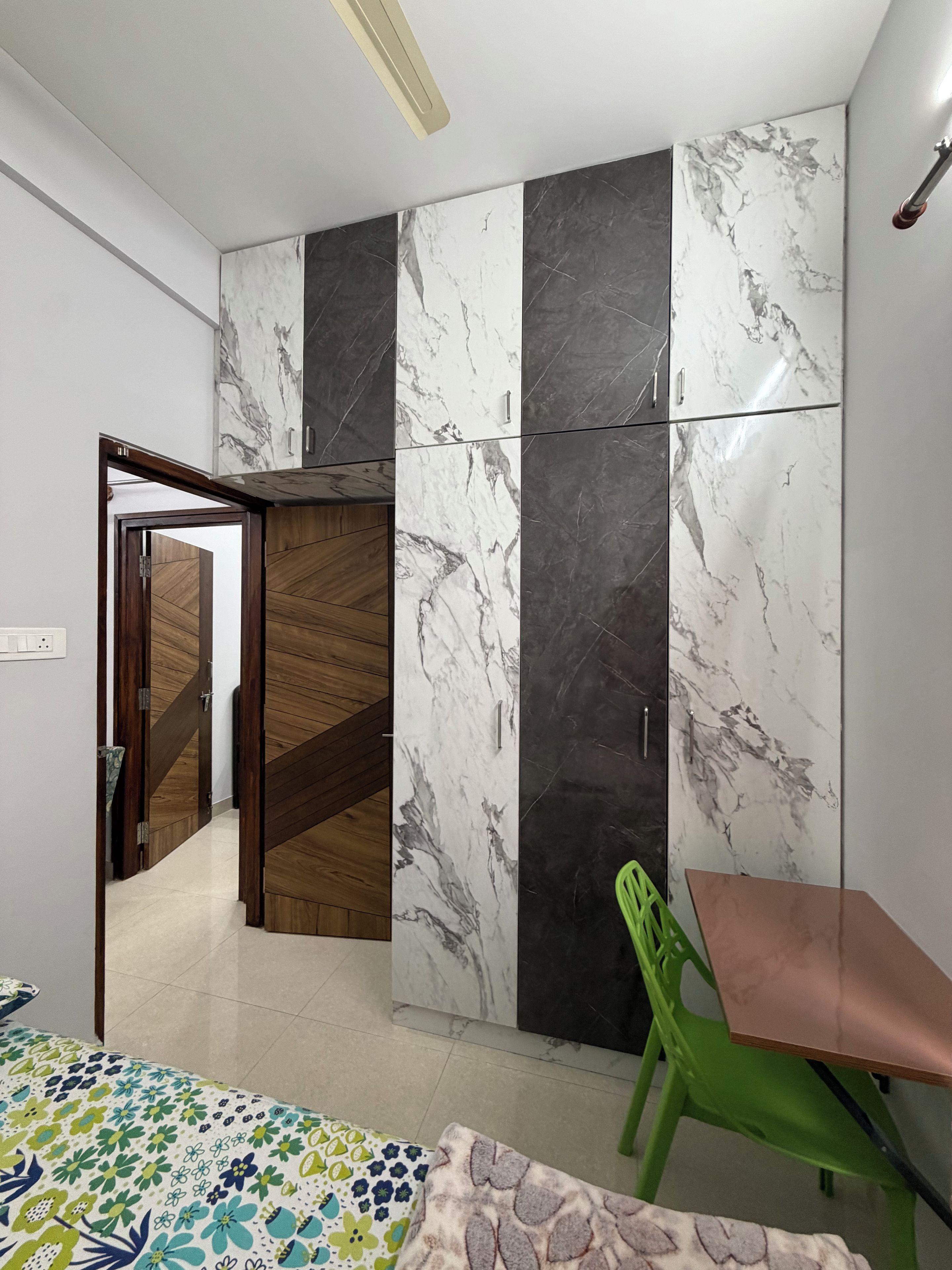 Ein Zimmer mit einem Kleiderschrank mit Marmorverkleidung, einer Holztür, einem grünen Sessel und einer bettenförmig gestreiften Tagesdecke.
