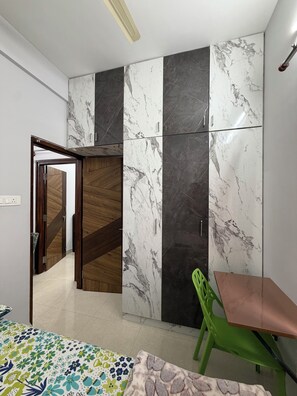 Een kamer met een inloopkast met marmeren panelen, een houten deur, een groene stoel en een bed met een decoratief sprei.