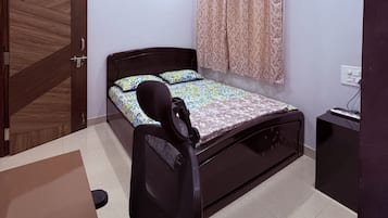 A bedroom with a bed, a desk, a chair, a ceiling fan, and a window with curtains.