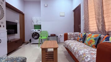 Ein Wohnzimmer mit einer Couch, einem Holztisch, einem Deckenventilator, einer Waschmaschine und einem Fernseher.