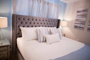 A neatly made bed with a tufted headboard, two bedside lamps, and a wall-mounted artwork. - Storey Lake 5BR Themed Rooms & Private Pool (Kissimmee)