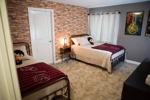 Une chambre avec deux lits, un mur en briques, une porte blanche, une table de chevet avec une lampe et une affiche accrochée au mur.