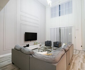 A modern living room with a sectional sofa, a flat-screen TV, and a glass coffee table. - Themed 5BR Near Disney Pool, Game Room (Kissimmee)