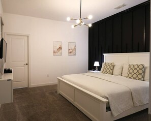 A bedroom with a bed, bedside table, lamp, and wall art. - Themed 5BR Near Disney Pool, Game Room (Kissimmee)