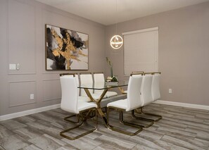 A dining area with a glass table, white chairs, a modern light fixture, and a large abstract painting on the wall. - Themed 5BR Near Disney Pool, Game Room (Kissimmee)