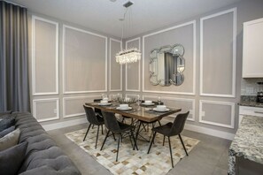 A dining area with a rectangular table set for four, surrounded by chairs, with a patterned rug on the floor. - 5BR Harry Potter Townhouse 15 min to Disney (Kissimmee)