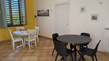A dining area with a round table and chairs, a white door, and a window with blinds.