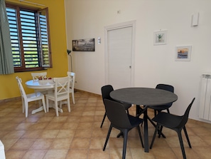 A dining area with a round table and chairs, a white door, and a window with blinds. - Residenza Don Alfonso (Somma Vesuviana)
