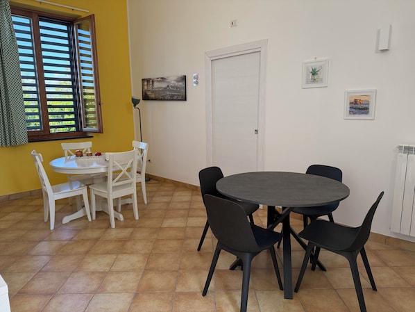A dining area with a round table and chairs, a white door, and a window with blinds.