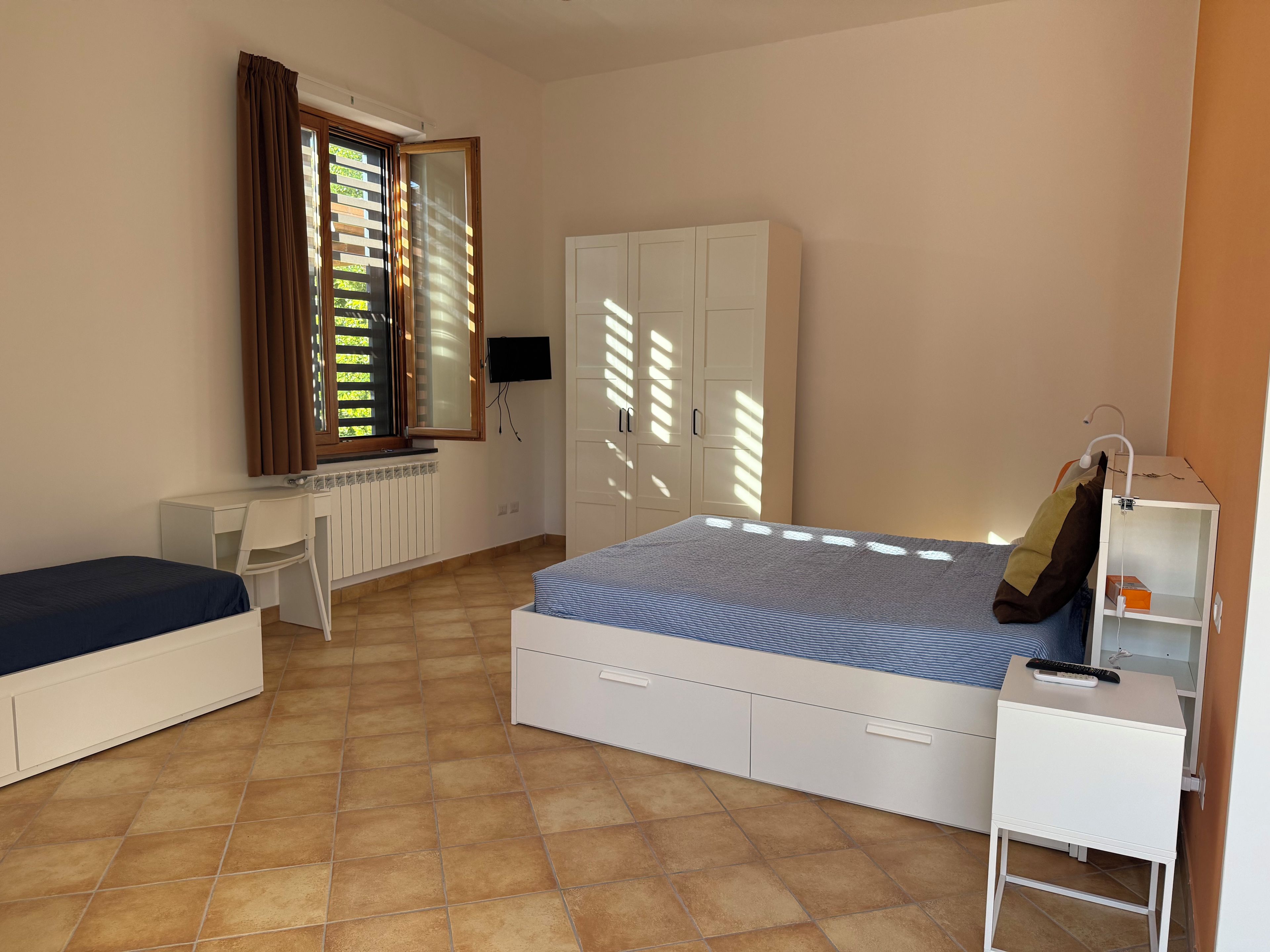 Ein Schlafzimmer mit einem Bett, einem Schreibtisch, einem Stuhl, einem Kleiderschrank und einem Nachttisch mit Lampe.