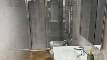 Ein modernes Badezimmer mit einer gläsernen Dusche, einem weißen Waschbecken und einem Holzkosmetikschrank.