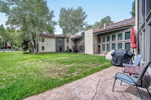 A courtyard with a grassy lawn, outdoor seating, and a building with large windows. - Charming Condo, Near BC/ Vail Resort, BBQ (Avon)
