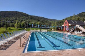 A swimming pool with multiple lanes, lounge chairs, and a red building in the background. - Charming Condo, Near BC/ Vail Resort, BBQ (Avon)