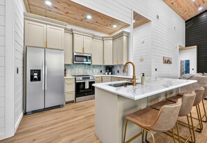 A modern kitchen with white cabinetry, stainless steel appliances, a marble countertop, and a bar area with stools. - EV Charger | Hot Tub | Sleeps 16 | Games (Broken Bow)