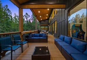 An outdoor deck with wicker furniture, a glass coffee table, and a view of the surrounding forest. - EV Charger | Hot Tub | Sleeps 16 | Games (Broken Bow)