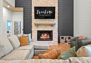 A living room with a stone fireplace, a mounted TV, and a sofa. - EV Charger | Hot Tub | Sleeps 16 | Games (Broken Bow)