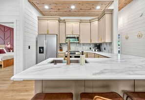 A modern kitchen with a marble island, stainless steel appliances, and wooden ceiling. - EV Charger | Hot Tub | Sleeps 16 | Games (Broken Bow)