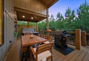 Une terrasse extérieure avec une table et des chaises en bois, un barbecue et un jacuzzi.