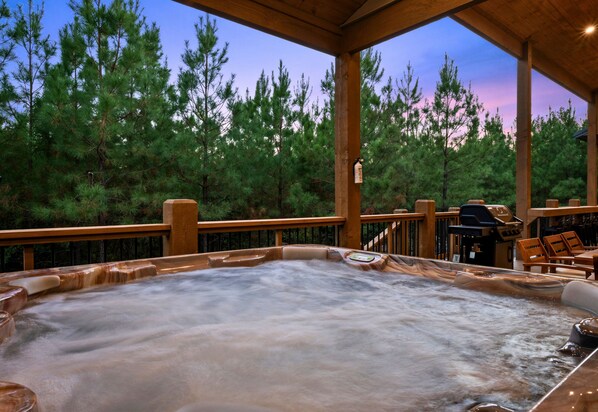 Un bain à remous avec une terrasse en bois et vue sur une forêt.