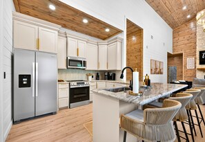 A modern kitchen with white cabinetry, stainless steel appliances, a marble countertop, and a wooden ceiling. - Children’s Playset | Hot Tub | Games | Sleeps 16 (Broken Bow)