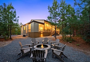 Eine Lodge mit Feuerstelle und Adirondack-Stühlen davor.